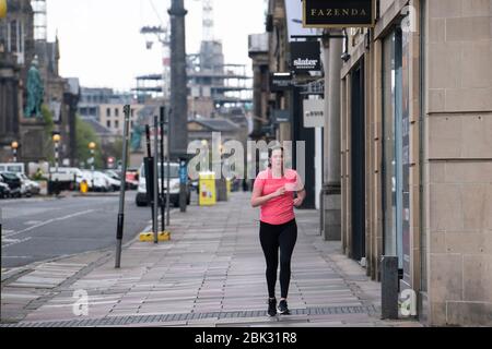 Edinburgh, Scotland, UK. 1 May 2020. Views of Edinburgh as coronavirus lockdown continues in Scotland. Streets remain deserted and shops and restaurants closed and many boarded up. Pictured; Closed shops and lone jogger on George Street.   Iain Masterton/Alamy Live News Stock Photo