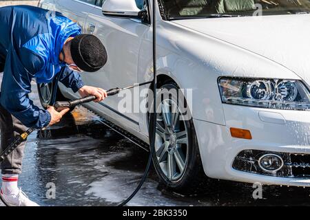 Professional washer in casual uniform washing luxury car with water gun on an open air car wash Stock Photo