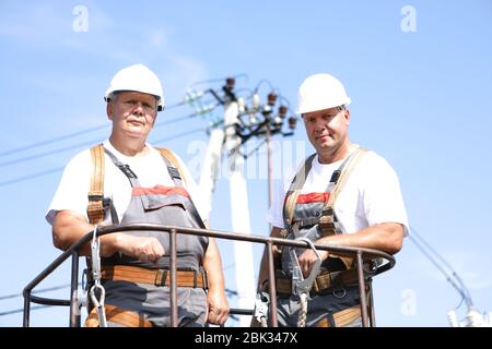 Two electrical workers on a lift. Engineers rise on a crane to repair a high-rise support. Men eliminate the accident at the high-altitude station Stock Photo