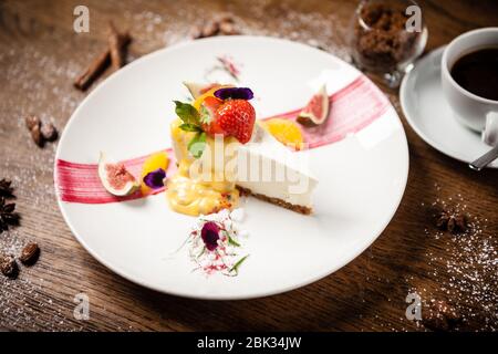 Cheesecake with passionfruit fig and orange sauce on a white plate. Delicious healthy gourmet dessert food closup served for dinner in restaurant. Stock Photo