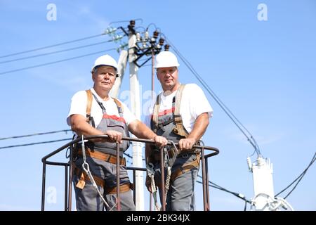 Two electrical workers on a lift. Engineers rise on a crane to repair a high-rise support. Men eliminate the accident at the high-altitude station Stock Photo