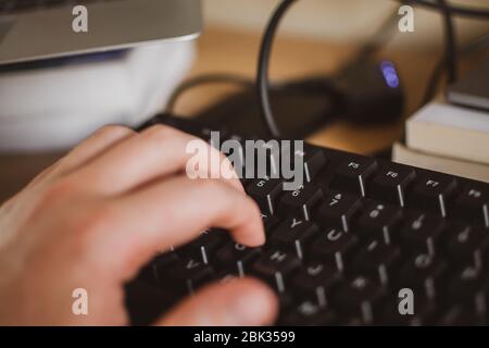 Close up of a person's hand typing on a keyboard in warm light whilst working from home during the COVID-19 lockdown Stock Photo