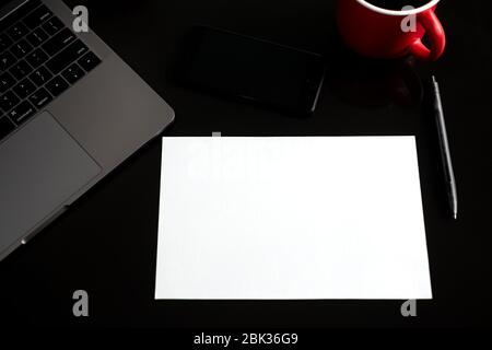 Toronto, Canada - 30, April, 2020: Blank paper with copy space, coffee cup, phone, laptop on black desk table. Top view, flat lay Stock Photo