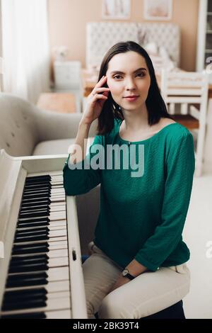 Cheerful lady sits on the chair near the white piano Stock Photo