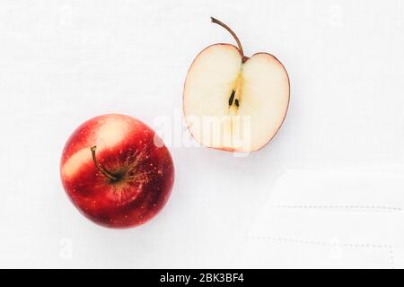 A whole two-color red apple Gala and halved red apple are placed on a white linen tablecloth. The photo is taken directly above. The main colors are r Stock Photo