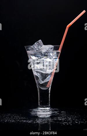 Clear drinking glass with ice and a orange plastic straw. Stock Photo