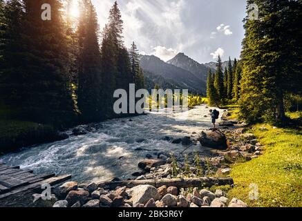 Tourist with big backpack near the river at green mountain valley in Karakol national park, Kyrgyzstan Stock Photo