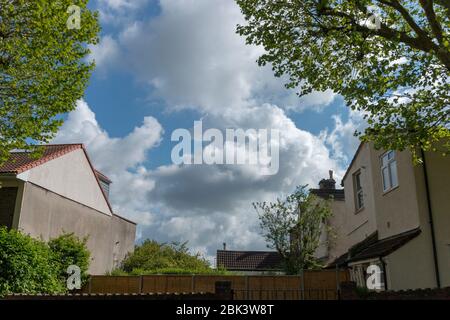 a close up view of the clouds in the blue sky though the middle of two buildings in a small village Stock Photo