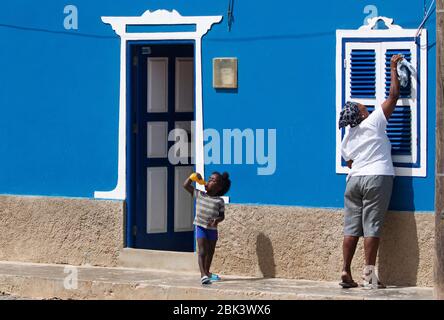Child and mother cleaning window shutters of blue coloured house in the village Bofareira / Bofarreira on island Boa Vista, Cape Verde / Cabo Verde Stock Photo