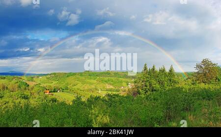 Spring rural rainbow landscape, view of green meadows and hills Stock Photo