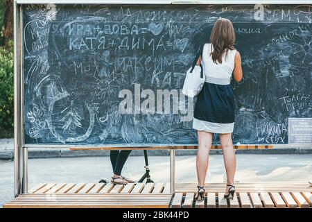 Moscow, Russia - AUGUST 9, 2014: Beautiful young girl in a short skirt and shoes writes on a chalk board in a park Sokolniki. Back view Stock Photo