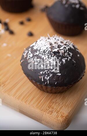 Chocolate glazed chocolate cocoa crazy cake muffins with coconut flakes in rows on a metal cooling rack Stock Photo