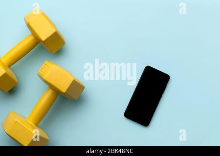 Flat lay top view yellow dumbbells and smartphone on blue background Stock Photo