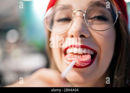 Young girl eating sweet sticky stick in France cafe in red beret and glasses. Concept caries and harm is danger to tooth enamel Stock Photo