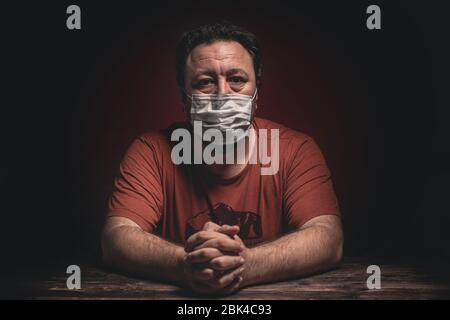 Attractive man with protective medical mask sitting desperate on the table looking worried, depressed, thoughtful and lonely suffering depression beca Stock Photo