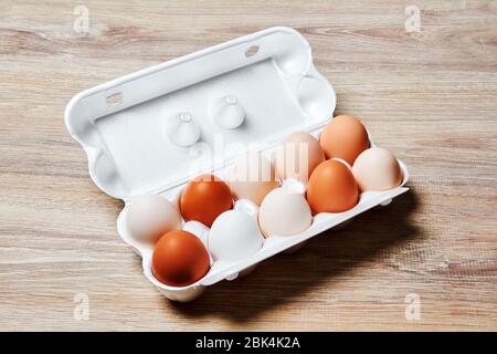 eggs of different shades from white to brown are packed together in one egg crate on a wooden table surface Stock Photo
