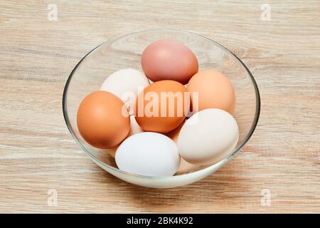 eggs of different shades from white to brown in a glass bowl on a wooden table surface Stock Photo