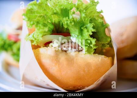 Burger is delicious American fast food, Closeup a hamburger made from pork or beef, green lettuce bread onion and tomato in a paper bag and plate on t Stock Photo