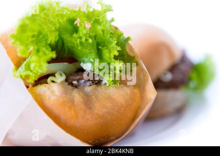 Burger is delicious American fast food, Closeup a hamburger made from pork or beef, green lettuce bread onion and tomato in a paper bag on a white tab Stock Photo