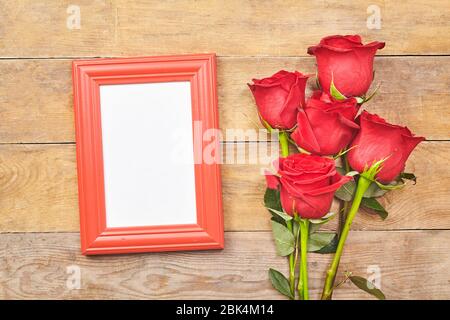 Red rose and blank photo frame on old wooden background. Top view. Stock Photo