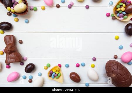 Easter background with chocolate eggs, easter bunny and other sweets on white wooden table with copy space Stock Photo