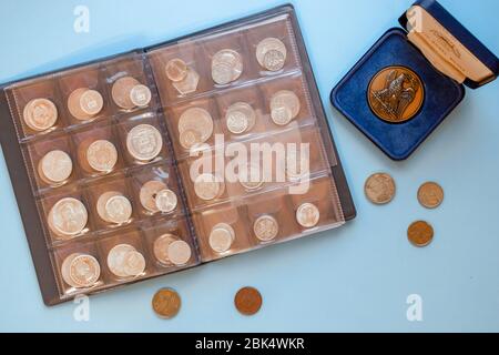 Numismatics. Old and expensive ancient collectible coins made of silver, gold and copper in a transparent plastic album on blue background. Top view. Stock Photo