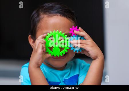 A hispanic boy having fun as he holds a gear set and learns about engineering in a exploratory problem solving environment. Stock Photo
