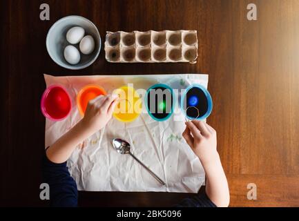 Overhead view of child's hands dying easter eggs on wooden table. Stock Photo