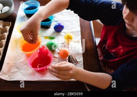 Close up of boy dipping an egg into dye to color it for easter. Stock Photo