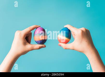Hands holding two brightly colored easter eggs against blue backdrop. Stock Photo