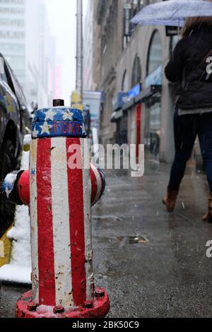 A woman holding an umbrella walks past a fire hydrant which is painted with the colours of the United States of America flag in Manhattan, midtown New Stock Photo