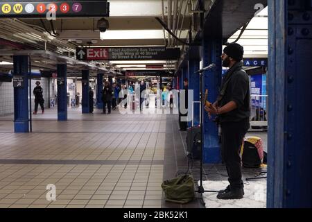 New York, NY / USA - December 29, 2019: Street performer singing and playing the guitar as subway commuters walk past Stock Photo