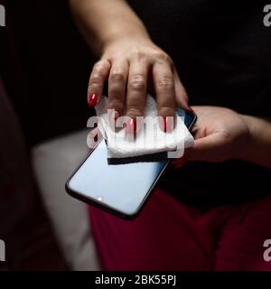 Female hands wiping mobile phone gadget with disinfectant wet wipe Stock Photo