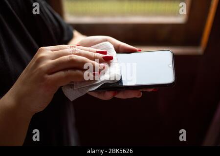 Female hands wiping mobile phone gadget with disinfectant wet wipe Stock Photo