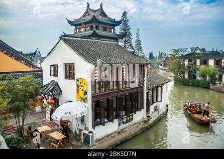 A boat passes a restaurant on the waterways of Zhujiajiao a watertown located in the Qingpu District of Shanghai, China. Stock Photo