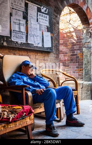 A worker resting in a chair in an alley in Shanghai’s Tianzifang area. Stock Photo