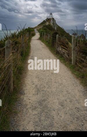 Nugget point lighthouse, Ahuriri flat, New Zealand - January 10, 2020 : The footpath to the Nugget point lighthouse on a moody and cloudy afternoon Stock Photo