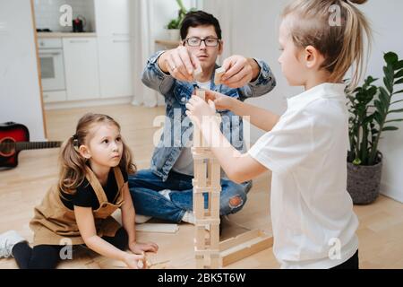 Dad and children playing building high tower from wooden blocks Stock Photo