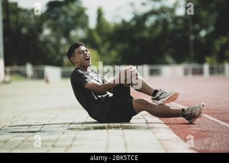 Handsome runner with muscular athletic body holding his leg with both hands Stock Photo
