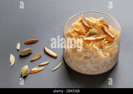 Vermicelli dessert, popular sweet dish know a kheer made with milk and garnish with dry fruits isolated on dark gray background, served in glass bowl. Stock Photo