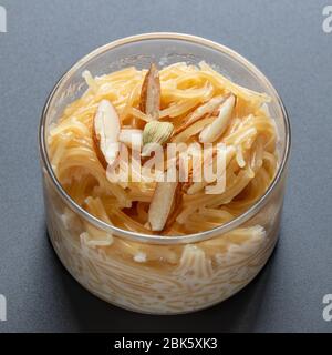 Vermicelli dessert, popular sweet dish know a kheer made with milk and garnish with dry fruits isolated on dark gray background, served in glass bowl. Stock Photo