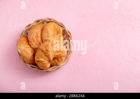 Top view croissants in the wooden basket on the pink background and texture. Stock Photo