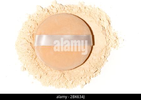 Scattered tan colored facial loose powder and puff on white background. Stock Photo
