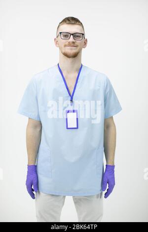 young male doctor or nurse in glasses and blue rubber gloves looks at camera Stock Photo