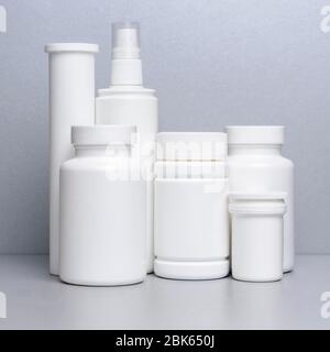5 white vials without labels for medicines, vitamins, sprays, liquids are on a gray shelf. mockup for pharmacy and store design Stock Photo