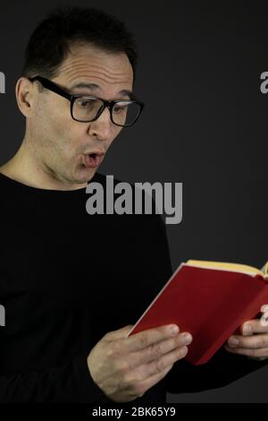 astonished handsome dark hair casual dressed 40s man in glasses reads book Stock Photo