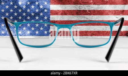Creative flag of the United States seen through a pair of eyeglasses lying on a white table Stock Photo