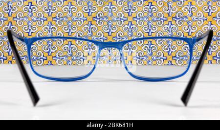 Azulejos tiled wall seen through a pair of blue eyeglasses lying on a white table Stock Photo