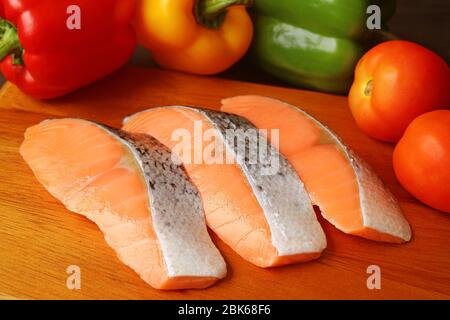 Closeup uncooked sliced salmons on a cutting board surrounded with colorful fresh vegetables Stock Photo
