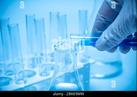 A researcher's hand holding a test tube containing blue liquid Stock Photo